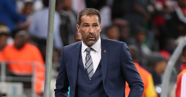 Male coach in a navy suit standing on the sideline during a game crowd in the background