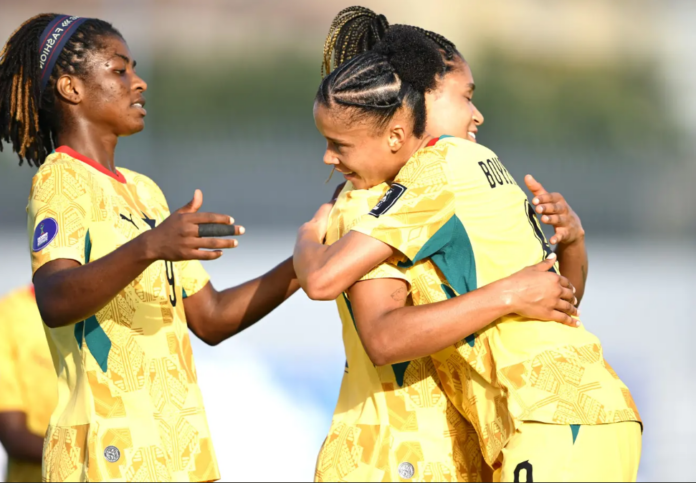 Three female soccer players in yellow uniforms celebrate sharing a group hug on the field
