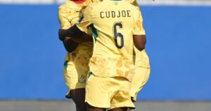 Soccer players in yellow uniforms embrace on the field showing the name CUDJOE and number 6 on one jersey