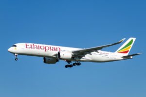 Ethiopian Airlines passenger jet in flight with landing gear extended against a clear blue sky tail fin with colorful Ethiopian logo visible on the right side of the plane
