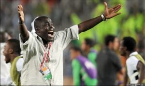 Celebrating man on a sports field with arms wide open and an ID badge around his neck