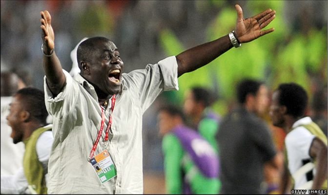 Celebrating man on a sports field with arms wide open and an ID badge around his neck