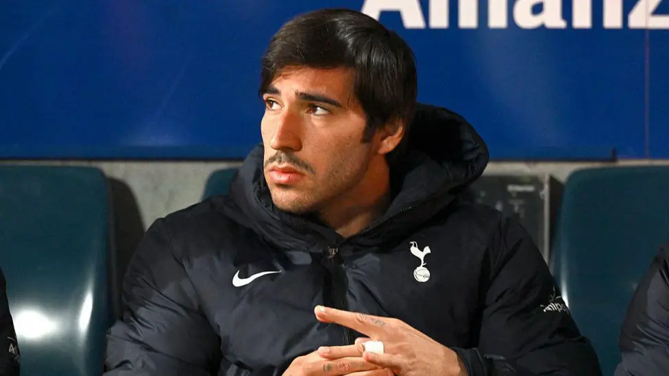 Man in a dark puffer jacket seated on a bench looking to his left