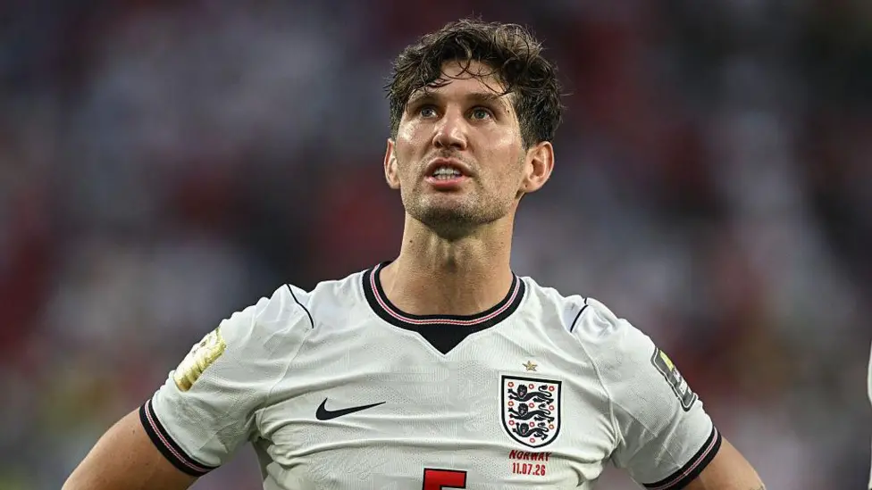England footballer in a white England shirt with crest looking up with hands on hips during a match