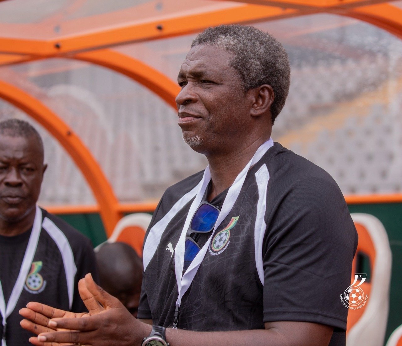 Football coach or official speaking at a dugout wearing black jersey and sunglasses hanging on chest