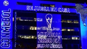 Blue neon lit building promoting the 2030 World Cup in South America with CONMEBOL branding and Se Juega En Casa text at the top