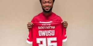 Smiling man holds up a red sports jersey with the number 25 against a beige wall