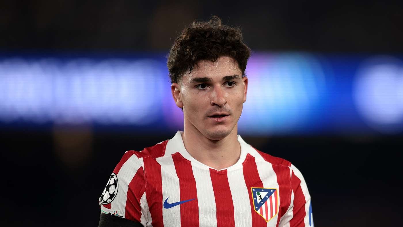 Football player in a red and white striped jersey with a Champions League badge facing forward on the pitch blue background lights behind him