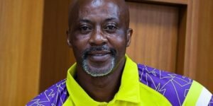 Smiling man wearing a bright yellow high visibility safety shirt with purple accents indoors in a wood paneled room