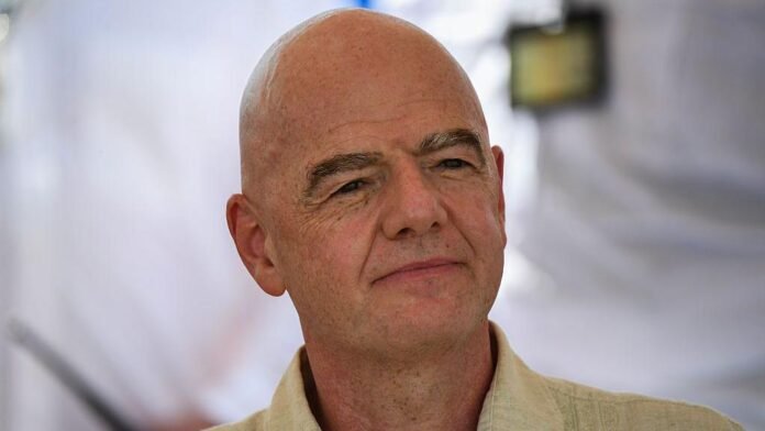 Bald light skinned man with a neutral expression wearing a beige shirt in a softly lit indoor setting