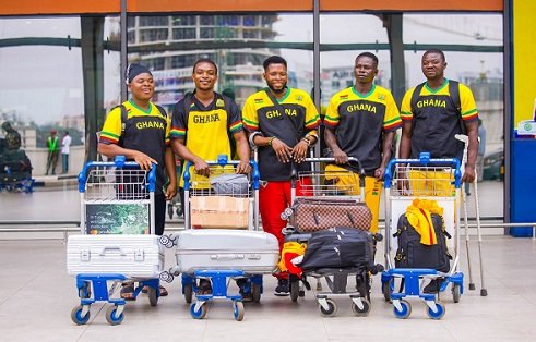 Ghana national football team players stand with luggage trolleys at an airport terminal posing for a photo