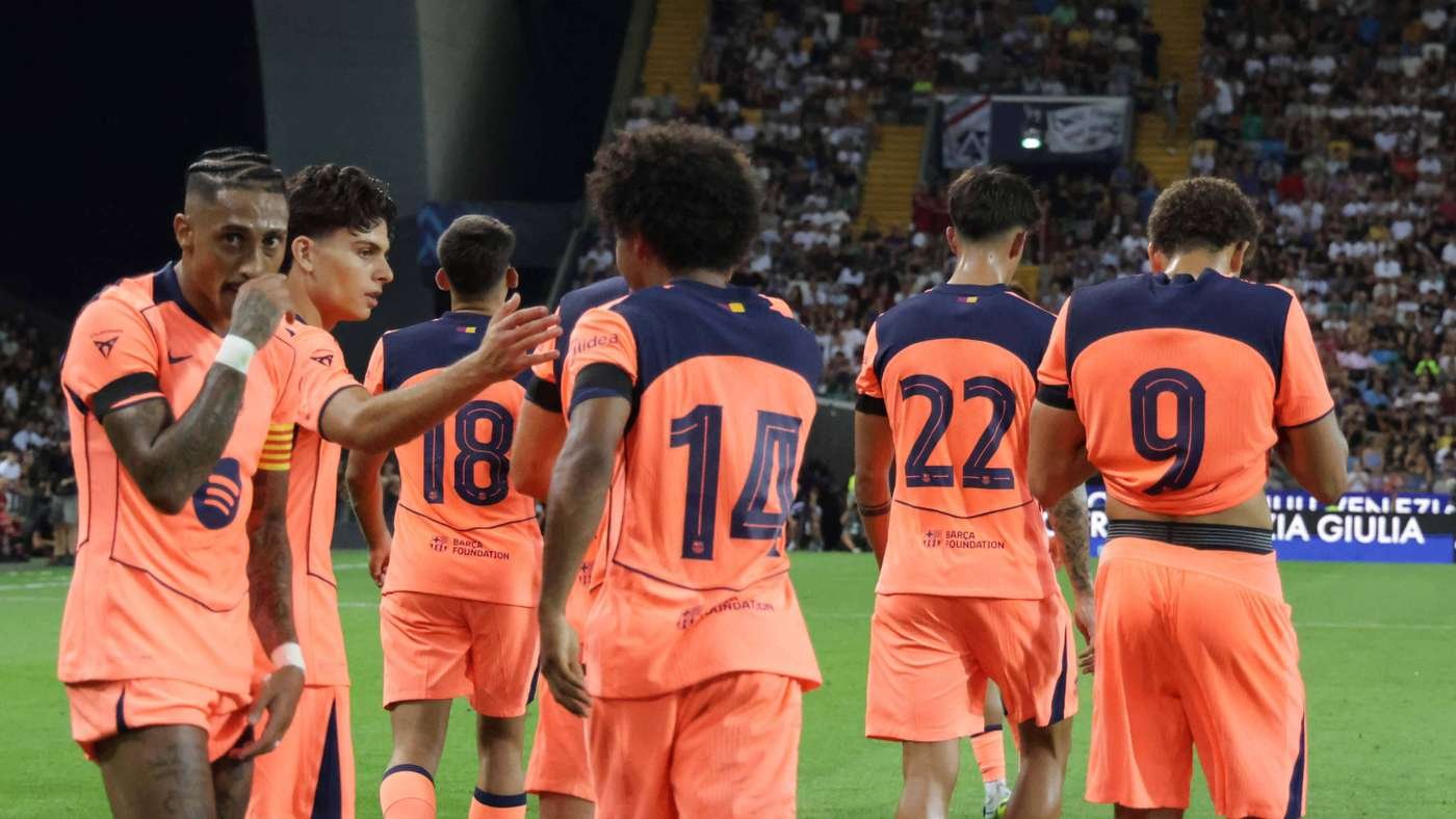 Soccer players in bright orange kits stand on a green pitch with their backs to the camera numbers 14 and 22 visible on their jerseys