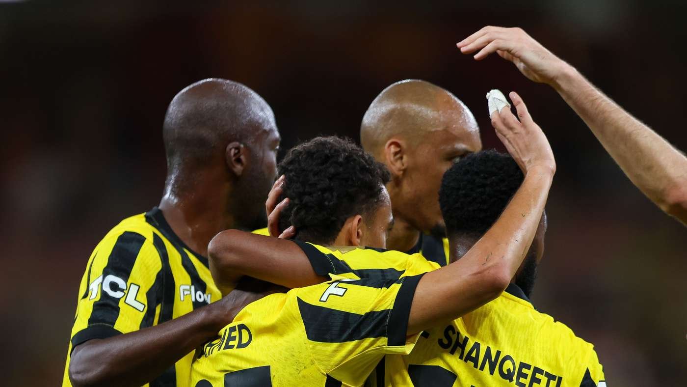 Soccer players in yellow and black celebrate with arms around each other in a group hug on the field