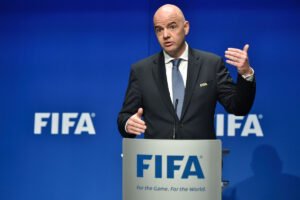 FIFA official in a dark suit speaks at a podium with the FIFA logo behind him