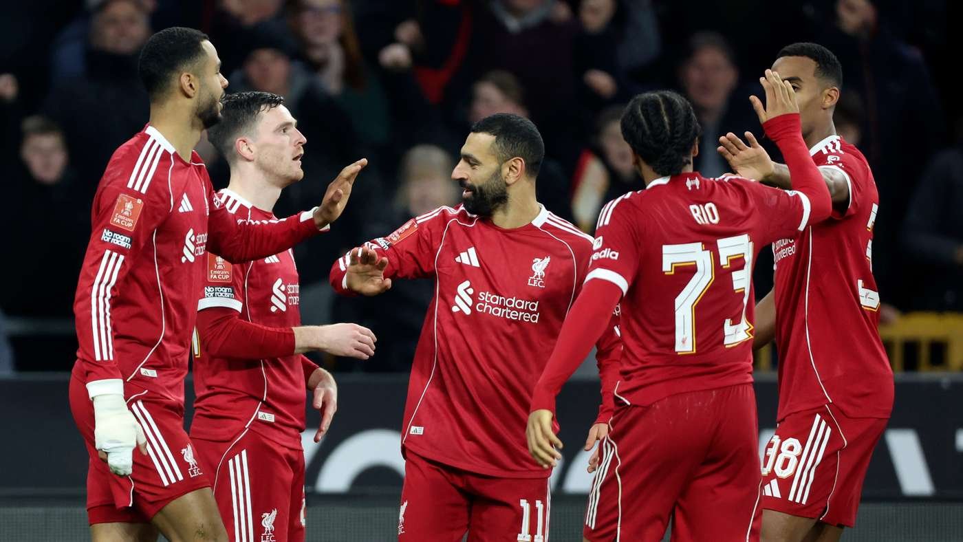 Liverpool FC players in red kits celebrate on the pitch high fiving and congratulating each other during a match with fans in the stands in the background