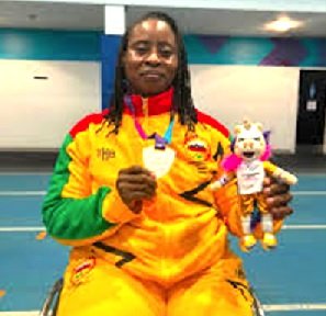 Athlete in a colorful tracksuit holds a medal and a plush mascot in a gymnasium