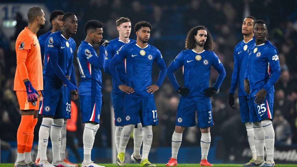 Chelsea FC players in blue kits stand in a line on the pitch before kickoff, with the goalkeeper in orange on the left.