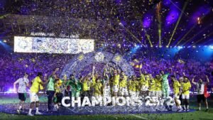 Soccer team in yellow jerseys celebrates on the field with confetti raining down and a large CHAMPIONS sign