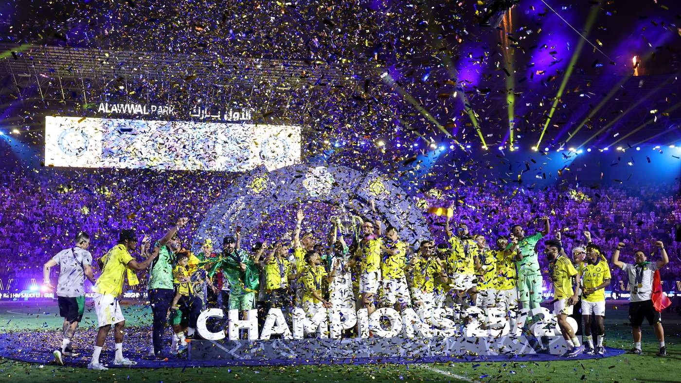 Soccer team in yellow jerseys celebrates on the field with confetti raining down and a large CHAMPIONS sign