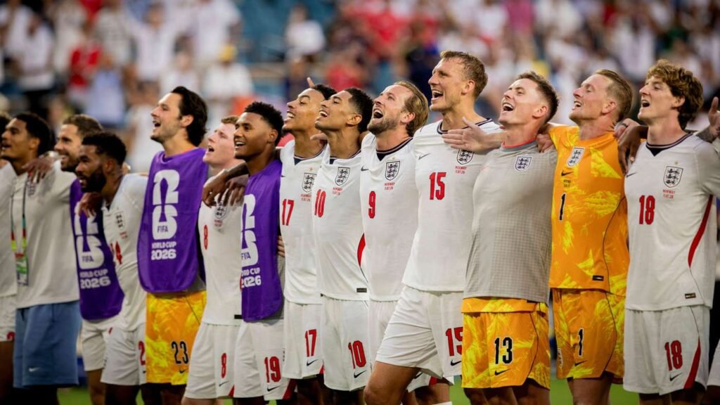 England men's football team players stand with arms around each other, celebrating on the pitch.