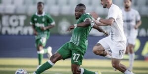 Soccer player in green 37 slides to intercept the ball as a white clad opponent pursues him on a sunny field