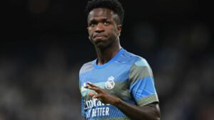 Soccer player in a Real Madrid blue kit on the field looking to the side with a focused expression and a hand raised slightly