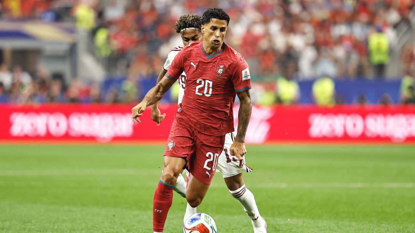 Portugal soccer player in red jersey number 20 dribbles the ball on a green field with a defender close behind