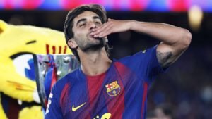 Barça player in blue red jersey blows a kiss in celebration trophy and mascot in the background