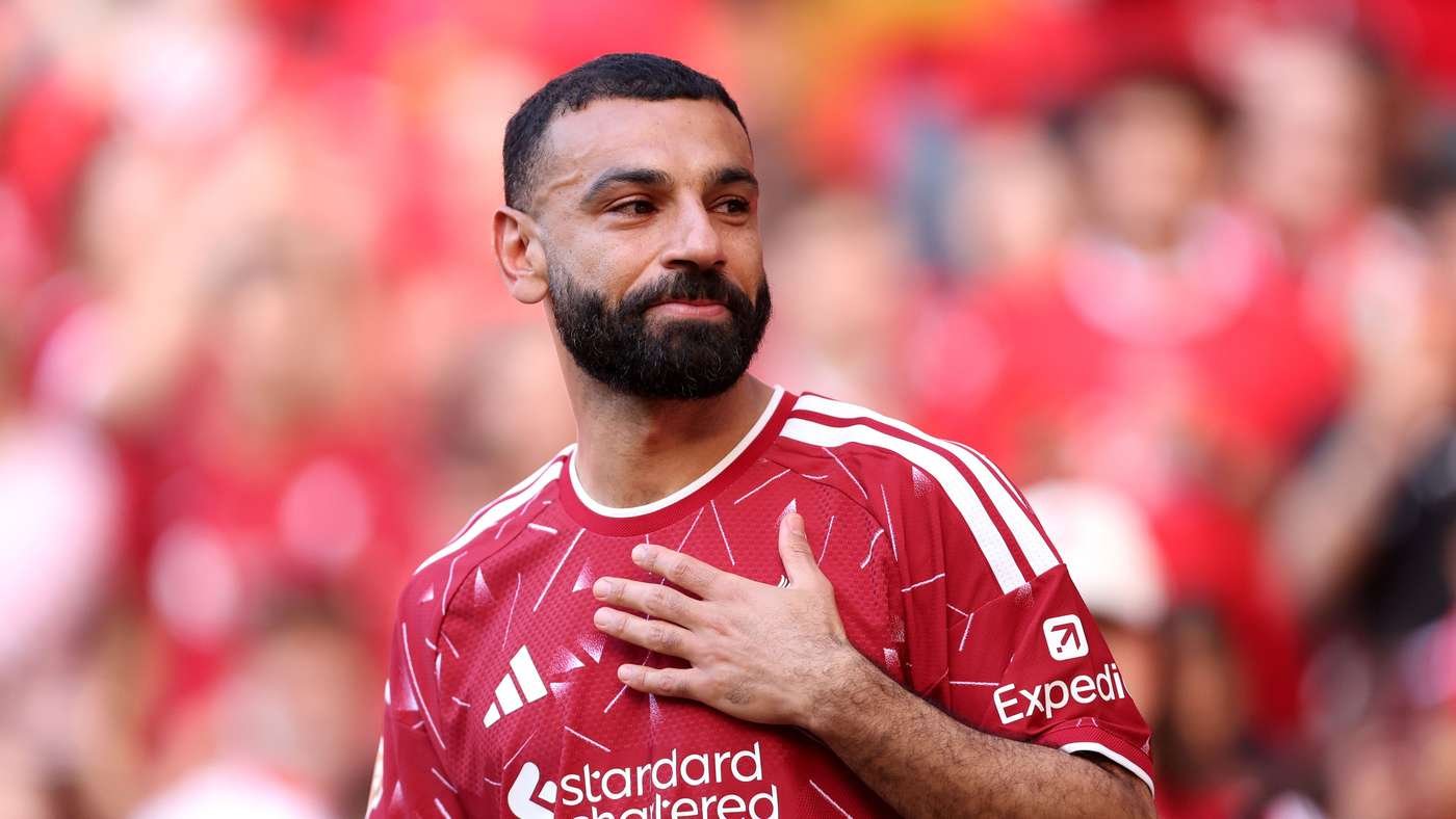 Bearded man in a red football jersey touching his chest standing among a sea of red clad fans