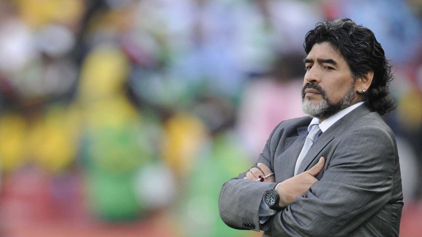 Man in a gray suit with arms crossed looking thoughtful against a colorful blurred background