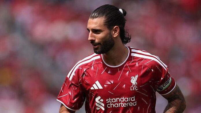 Professional footballer with dark hair tied back wearing a red Liverpool FC jersey with captains armband on the pitch