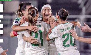 Female soccer players in white uniforms celebrate together with smiles on a field
